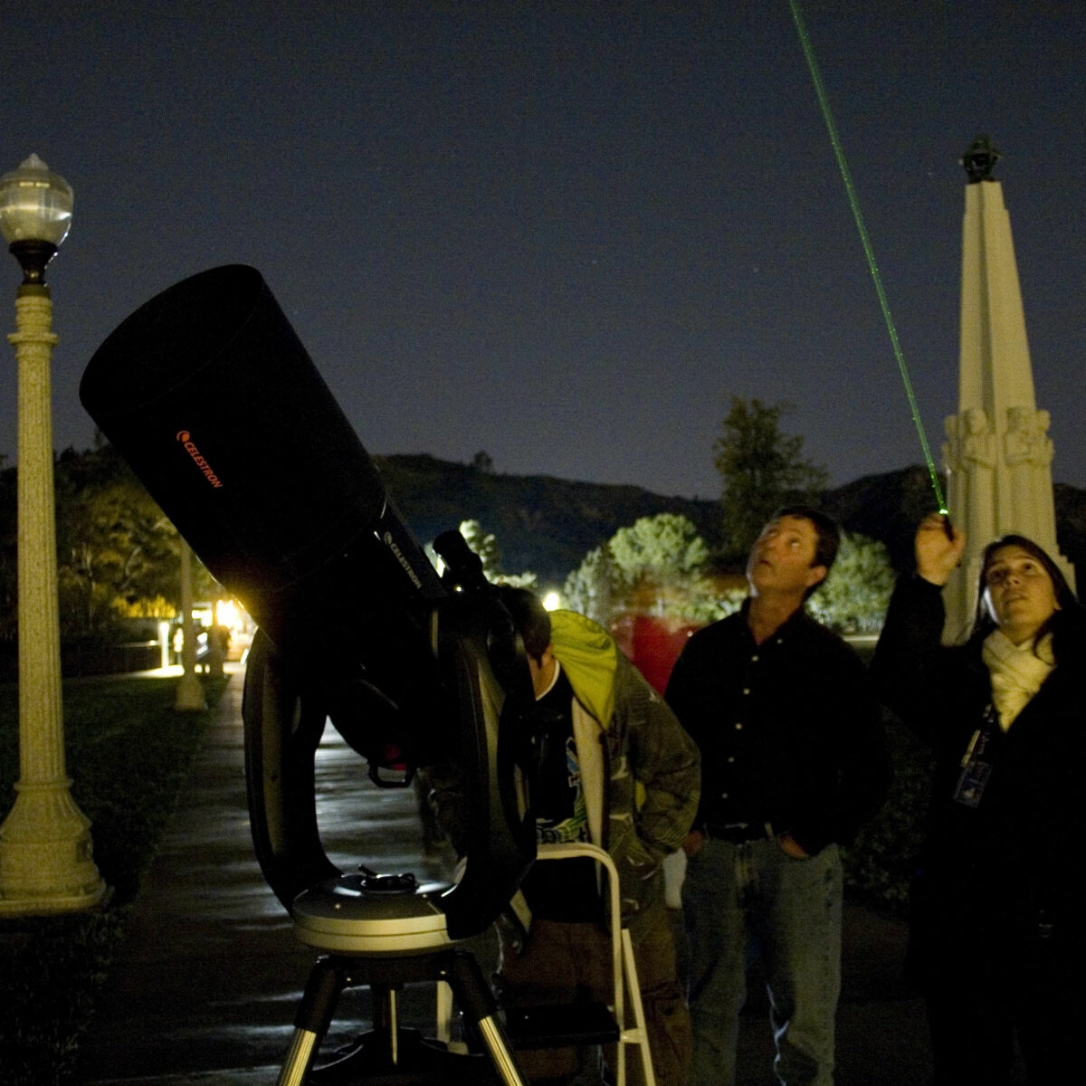 Telescope demonstrator Katy Haugland uses a laser to point out celestial wonders to Observatory patrons while standing next to a telescope on the lawn.