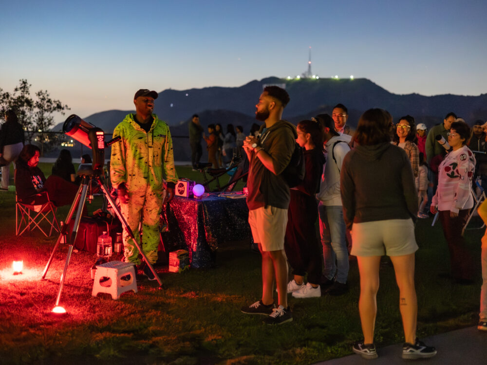A Telescope Demonstrator greets a line of people waiting to look through the lawn telescope.