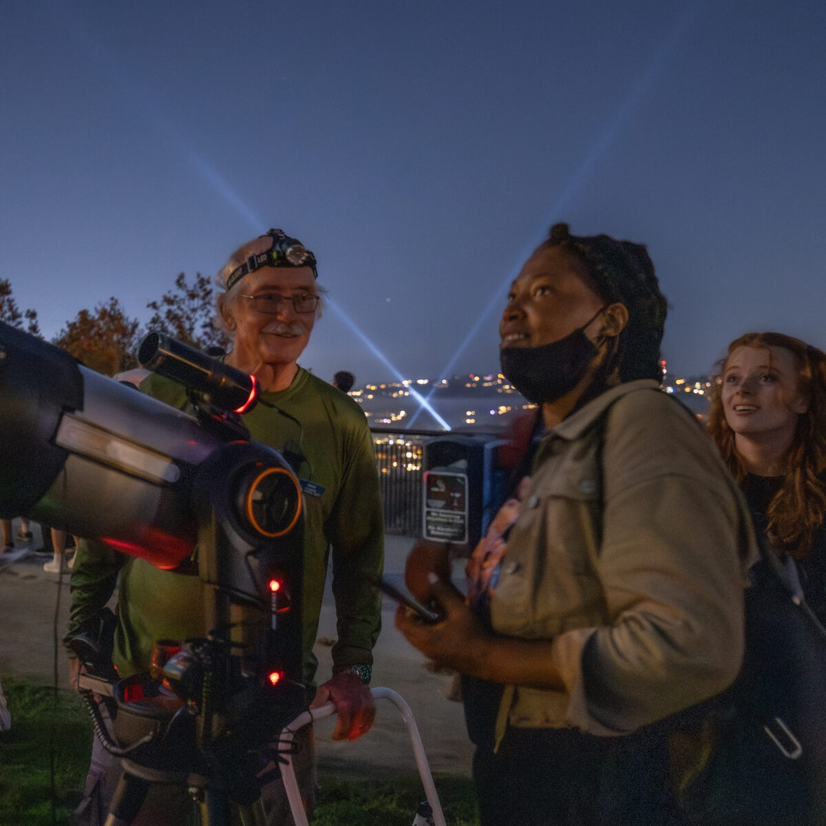 People looking up at the night sky with a telescope in the foreground.