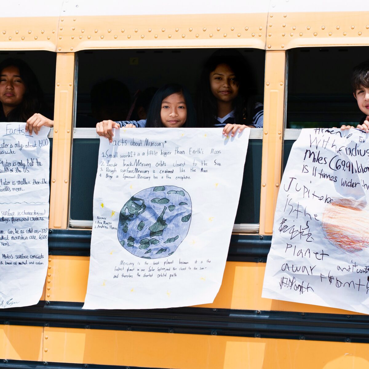 Kids hanging handmade planet posters from the school bus windows.